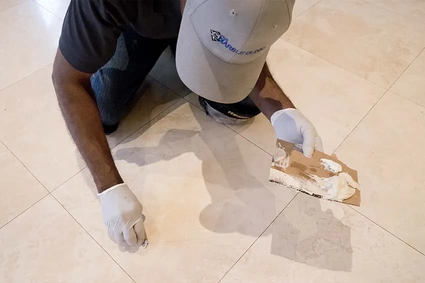 Technician filling a chip in a stone floor with epoxy