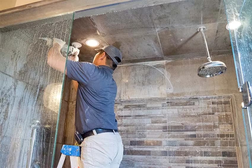 Technician polishing stone shower walls behind a glass door