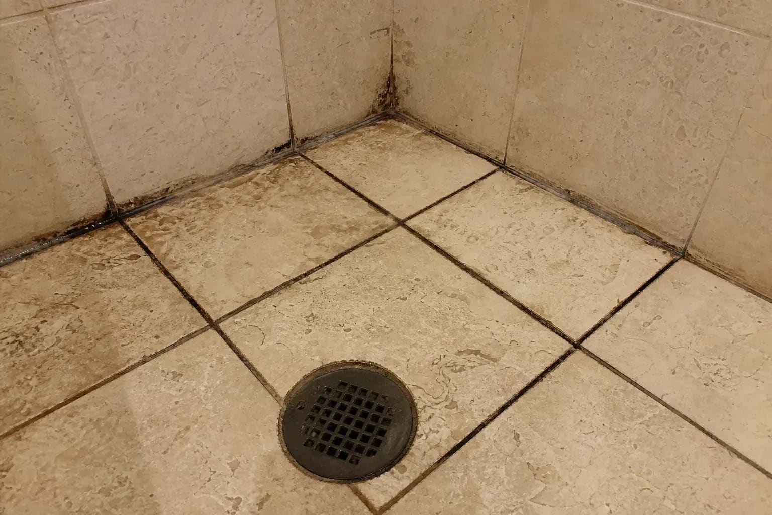 Shower floor with dark stained grout lines and soap scum between stone tiles