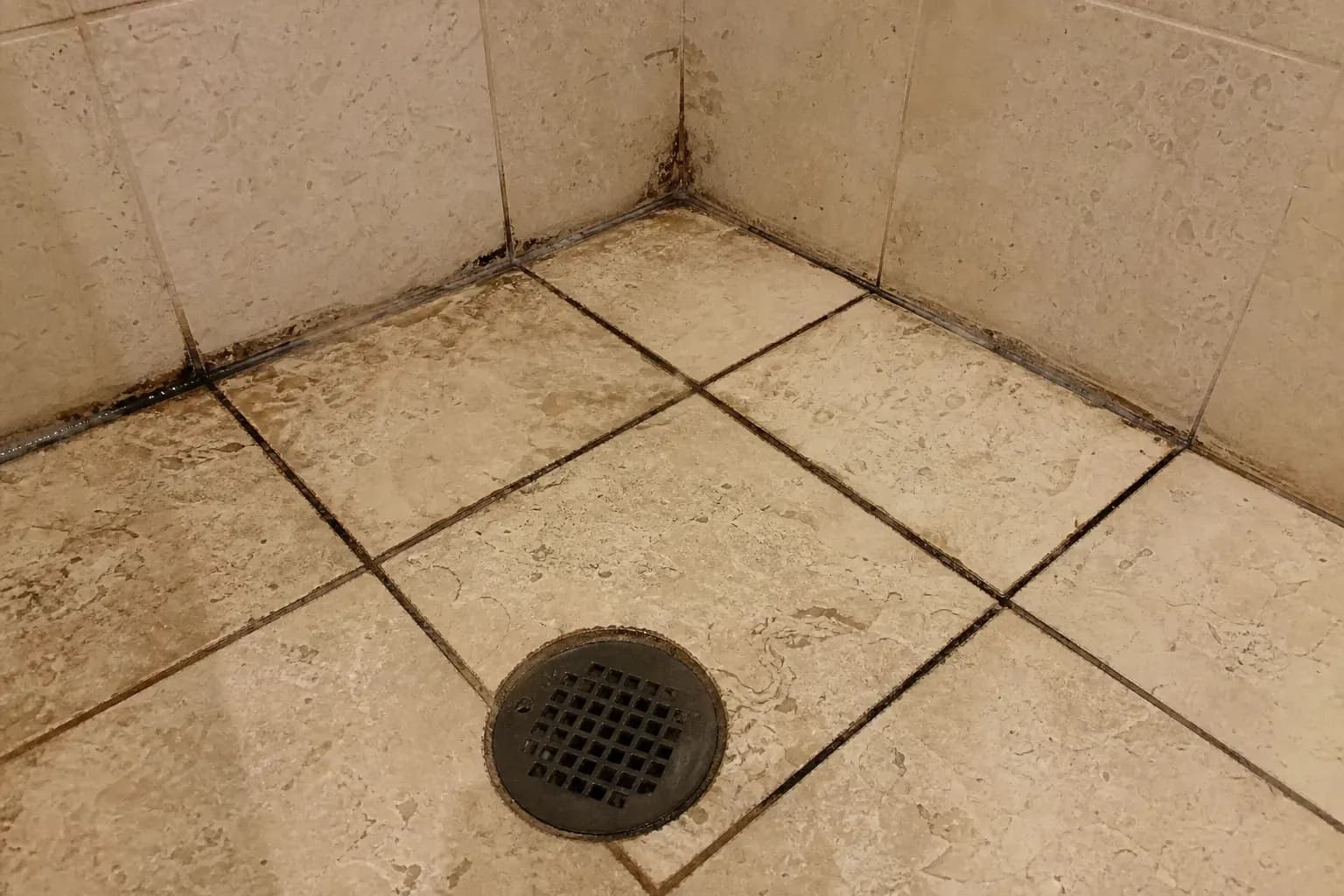 Shower floor with dark stained grout lines and soap scum between stone tiles